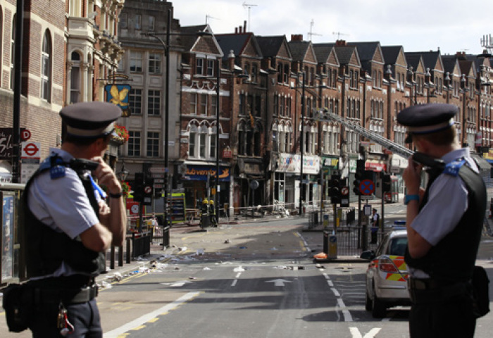 Police officers stand near a burnt out shop in Clapham Junction, in south London August 9, 2011. British Prime Minister David Cameron said he would recall parliament from its summer recess for a day on Thursday after rioting swept through London for three consecutive nights.