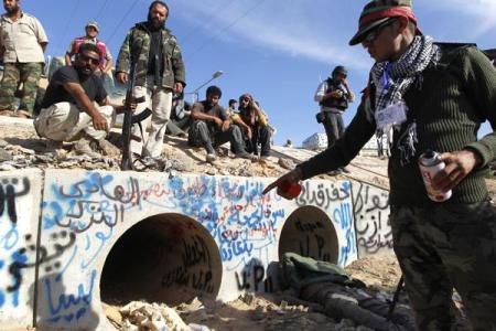 An anti-Gaddafi fighter points at the drain where Muammar Gaddafi was hiding before he was captured in Sirte, Libya on Oct. 20, 2011.