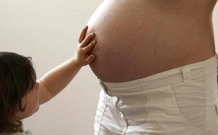 A child touches a pregnant mother's stomach.