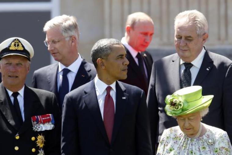 Red light reflected from the carpet illuminates Russian President Vladimir Putin as he passes President Obama and other leaders at a group photo for the 70th anniversary of the D-Day landings in Benouville June 6, 2014.