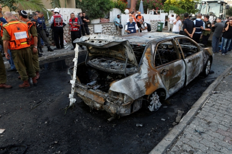 Israeli firefighters, medics and soldiers from the Home Front Command stand next to a burnt car at the scene after a rocket fired by Palestinian militants in Gaza landed in the southern town of Kiryat Gat July 31, 2014.