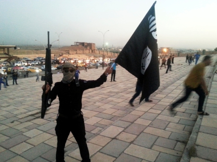 A fighter of the Islamic State of Iraq and the Levant holds an ISIL flag and a weapon on a street in the city of Mosul, June 23, 2014.