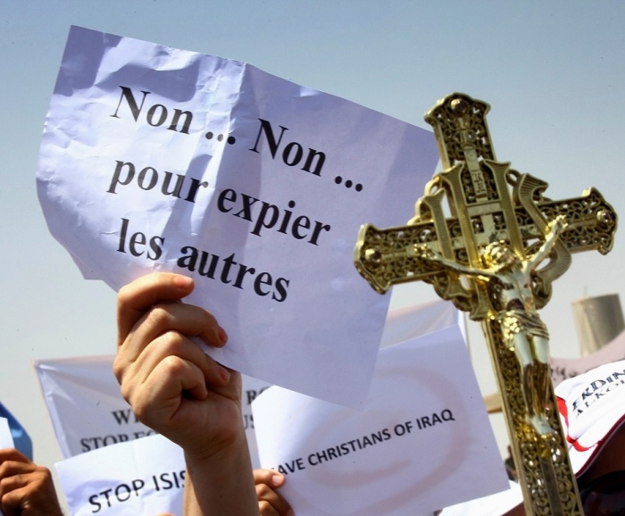 A protester carries a cross during a demonstration against militants of the Islamic State, formerly known as the Islamic State in Iraq and the Levant in Arbil, north of Baghdad July 24, 2014. The sign reads as 'No... no... to atone others.'