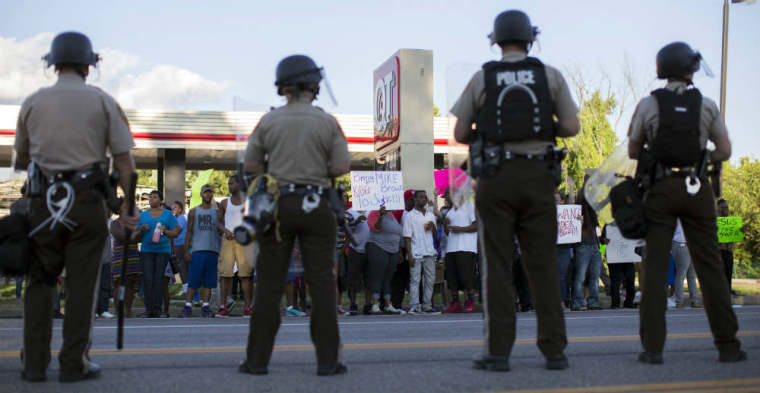 Police officers watch as demonstrators protest the death of black teenager Michael Brown in Ferguson, Missouri August 12, 2014.