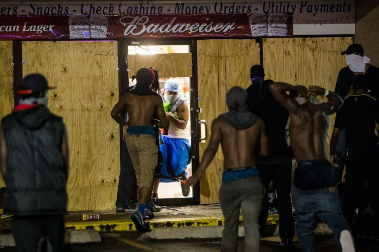 A masked man carries items out of a liquor store that had been broken into during on-going demonstrations to protest against the shooting of Michael Brown, in Ferguson, Missouri, August 16, 2014. Protesters in Ferguson said late on Friday on Twitter that police had fired tear gas at a crowd protesting over the police shooting death of Brown, an unarmed black teen. The reported outbreak late Friday evening came after almost a week of nighttime clashes between local police and protesters saw a 24-hour break as those police forces were replaced by state police led by an African-American captain.