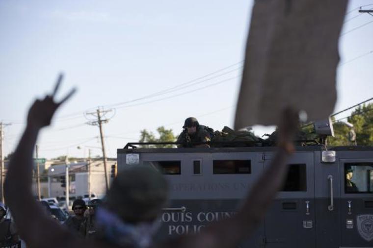 A police officer aims his weapon at a demonstrator protesting the shooting death of teenager Michael Brown, in Ferguson, Missouri, Aug. 13, 2014.