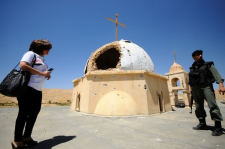 A woman and a soldier loyal to Syria's president Bashar Al-Assad stand beside a damaged church in Maaloula, Syria, August 21, 2014. Residents of Maaloula, a Christian town in Syria, call on other Christian groups and minorities to stand up to the radicalism that is sweeping across Syria and Iraq. The town was regained by Syrian Army forces in April from Islamic militants, and several months later life is slowly returning to the town.