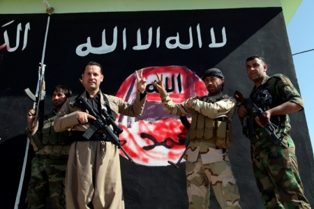 Kurdish Peshmerga fighters pose near a wall on which the black flag commonly used by Islamic State militants has been painted over, in the northern Iraqi town of Zumar, October 26, 2014, after having taken it from Islamic State. Kurdish forces retook Zumar and several nearby villages from Islamic State early on Saturday after heavy coalition air strikes against the Islamist insurgents, security sources said.