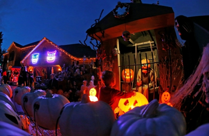 A visitor to a house covered in Halloween decorations looks over the scene in the front yard in the Chicago suburb of Naperville, Illinois, October 27, 2014. Breathtaking purple-and-orange light displays, zombie graveyards, mutilated mannequins and singing inflatable pumpkins are just some of the front-yard Halloween decorations that Americans are expected to spend $7.4 billion on this year. In the Chicago suburb of Naperville, the displays got so elaborate that Annette Wehrli decided to set up a tour. Wehrli's Naperville Trolley & Tours, which has run tours of Christmas lights for 19 years, put Halloween on the schedule at the suggestion of enthusiastic residents of the sprawling upper middle-class city of 200,000.