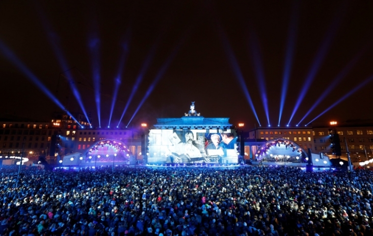 German actor Jan Josef Liefers speaking to singer-songwriter and former GDR dissident Wolf Biermann is seen on the right side of the video screen while an early picture of Biermann is seen at left at the Brandenburg Gate in Berlin, November 9, 2014. Germany on Sunday marks the 25th anniversary of the fall of the Berlin Wall.