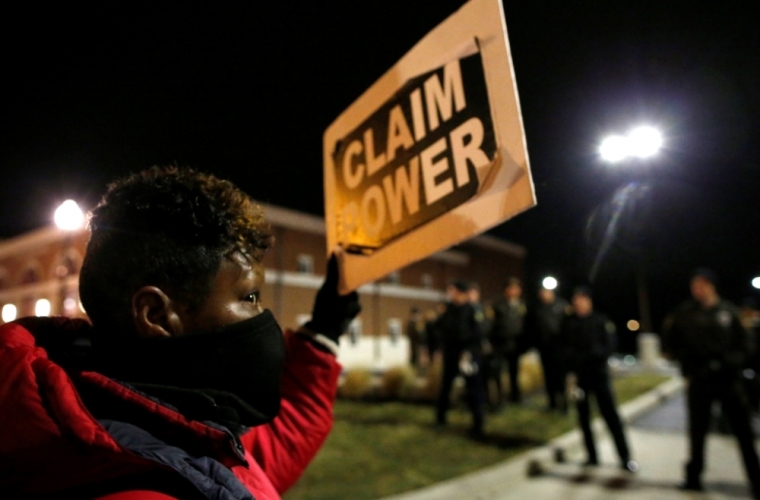 A protester holds a sign outside the Ferguson Police Department in Ferguson, Missouri, November 24, 2014. Missouri Governor Jay Nixon urged people in the St. Louis area to show respect and restraint following a grand jury's decision on whether to criminally charge a white police officer in the August fatal shooting of unarmed black teenager Michael Brown.Prosecutors are set to announce the grand jury's decision at 8 p.m. on Monday.