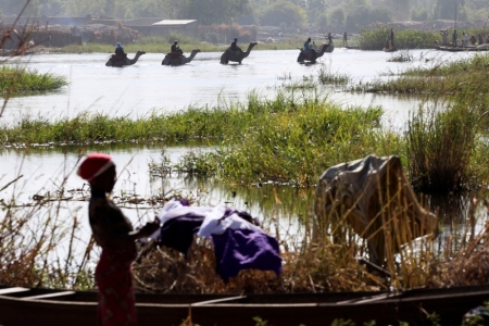 Men on camels cross the water as a woman washes clothes in Lake Chad in Ngouboua, January 19, 2015. Refugees fleeing attacks by Islamist militant group Boko Haram continued to cross the border into neighbouring Chad on Monday. According to United Nations and government figures, some 20,000 Nigerians had fled to Chad, Niger and Cameroon in the two weeks prior to January 13 after their towns and villages were attacked. .