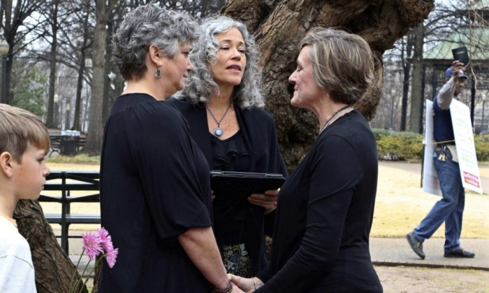 A couple identified as only Donna and Tina get married as a protester waves a Bible in a park outside the Jefferson County courthouse in Birmingham, Alabama.