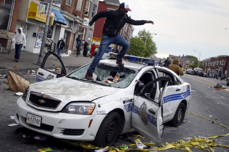 Demonstrators jump on a damaged Baltimore police department vehicle during clashes in Baltimore, Maryland, April 27, 2015. Several Baltimore police officers were injured on Monday in violent clashes with young people after the funeral of a black man, Freddie Gray, who died in police custody, and local law enforcement warned of a threat by gangs.