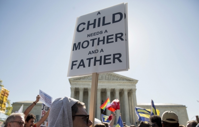 A protester holds a sign against same sex marriage in front of the Supreme Court before the court hears arguments about gay marriage in Washington, April 28, 2015. The nine justices of the Supreme Court began on Tuesday to hear arguments on whether the Constitution provides same-sex couples the right to marry, taking up a contentious social issue in what promises to be the year's most anticipated ruling.