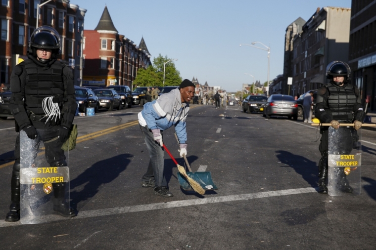 A man cleans up Pennsylvania avenue as Maryland State police stand guard Monday in Baltimore, Maryland, April 28, 2015. Baltimore erupted in violence on Monday as hundreds of rioters looted stores, burned buildings and at least 15 police officers were injured following the funeral of Freddie Gray, a 25-year-old black man who died after suffering a spinal injury in police custody. The riots broke out blocks from where the funeral of Gray took place and spread through much of west Baltimore.