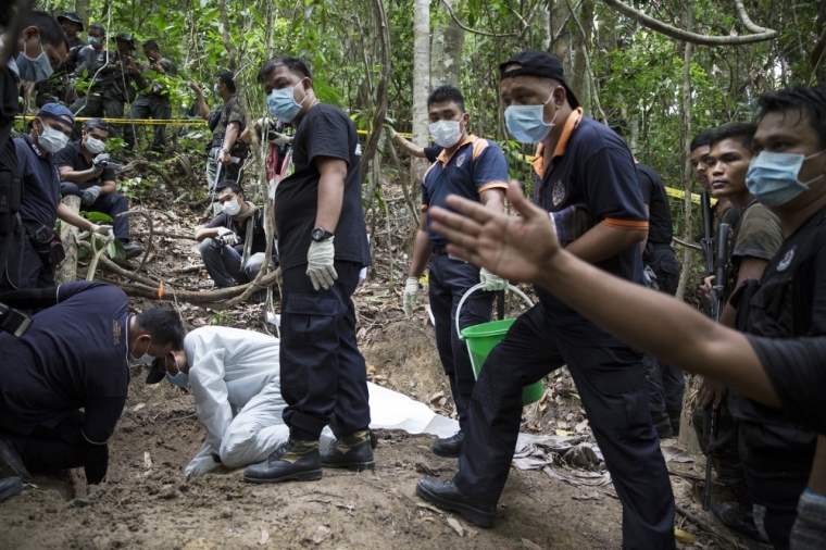 Policemen monitor as forensic experts dig out human remains near the abandoned human trafficking camp in the jungle close the Thailand border at Bukit Wang Burma in northern Malaysia, May 26, 2015. Malaysian police forensic teams, digging with hoes and shovels, began the grim task on Tuesday of exhuming the bodies of dozens of suspected victims of human traffickers found buried around jungle camps near the Thai border.