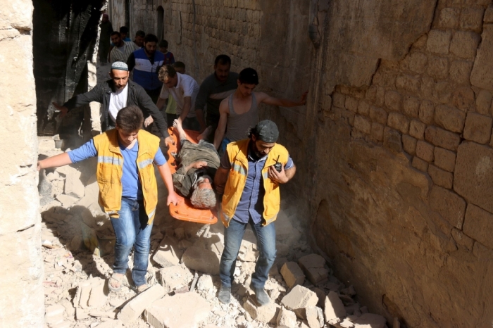 Members of the Civil Defence carry an injured man on a stretcher as they walk upon rubble at a site hit by what activists said was a barrel bomb dropped by forces of Syria's President Bashar al-Assad, in the old city of Aleppo, May 31, 2015.