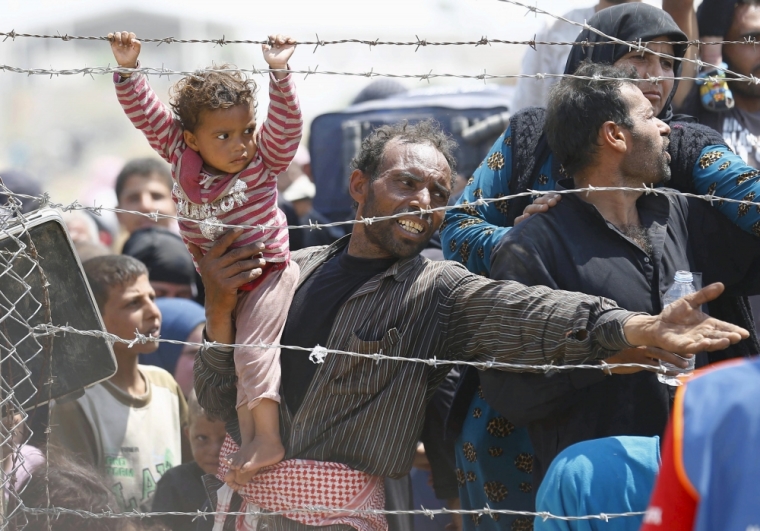 A Syrian refugee holds onto his daughter as he pleads to cross into Turkey at Akcakale border gate in Sanliurfa province, Turkey, June 15, 2015.