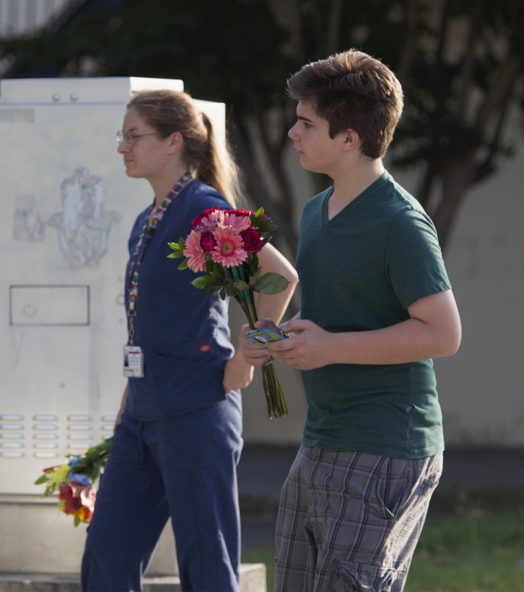 Charleston residents Darby Jenkins (R) and his mother Ashley, look for a spot to leave flowers for the victims of Wednesday's shootings, near a police barricade in Charleston, South Carolina, June 18, 2015. Police in Charleston were searching for a white gunman on Thursday who killed nine people in a historic African-American church, in an attack that police and the city's mayor described as a hate crime.