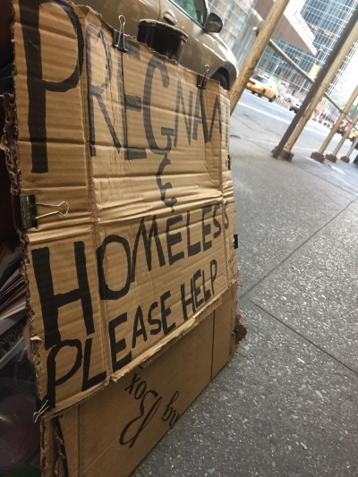 A young homeless person begs for money on the streets with a sign that read 'pregnant and homeless.'