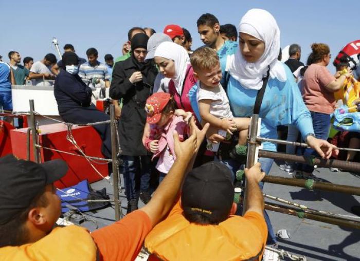 Members of the Turkish coast guards help a Syrian migrant family to disembark on the shore in Cesme, near the Aegean port city of Izmir, Turkey, August 11, 2015.