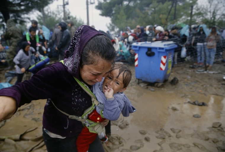 A Syrian refugee cries as she carries her baby walking through the mud to cross the border from Greece into Macedonia during a rainstorm, near the Greek village of Idomeni, September 10, 2015.