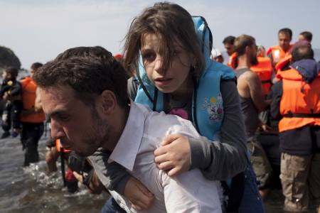 A Syrian refugee carries a young girl moments after arriving on a dinghy on the Greek island of Lesbos, September 10, 2015. Most of the people flooding into Europe are refugees fleeing violence and persecution in their home countries who have a legal right to seek asylum, the United Nations said on Tuesday.