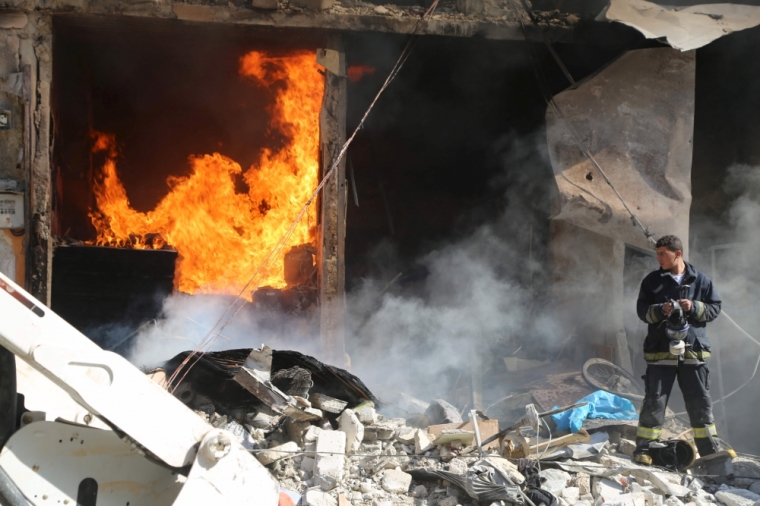 A Civil Defence member carrying a gas mask stands amid debris near a fire caused by what activists said was a barrel bomb dropped by forces loyal to Syria's president Bashar Al-Assad in Aleppo's al-Saliheen district, May 1, 2015.