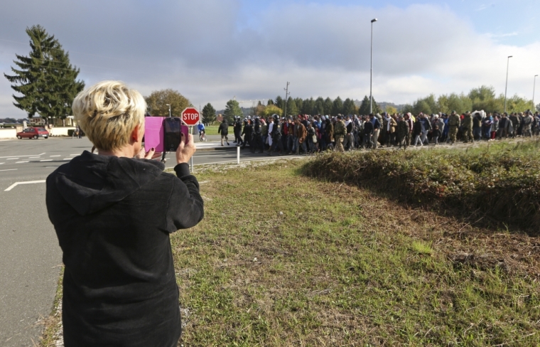 A woman uses a mobile device to take photos of migrants as they walk in Dobova, Slovenia, October 20, 2015. Migrants continue to stream north through the Balkans from Greece but Hungary sealed its border with Croatia on Friday and Slovenia imposed daily limits on migrants entering from Croatia, leaving thousands stuck on cold, rain-sodden frontiers.