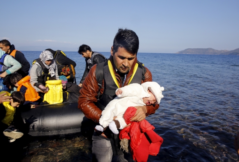 An Afghan migrant carries his one-month-old child as he disembarks from an overcrowded raft at a beach on the Greek island of Lesbos, October 19, 2015. Thousands of refugees - mostly fleeing war-torn Syria, Afghanistan and Iraq - attempt daily to cross the Aegean Sea from nearby Turkey, a short trip but a perilous one in the inflatable boats the migrants use, often in rough seas. Almost 400,000 people have arrived in Greece this year, according to the U.N. refugee agency UNHCR, overwhelming the cash-strapped nation's ability to cope.