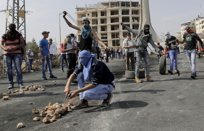 Palestinian protesters use slings to hurl stones towards Israeli troops during clashes near the Jewish settlement of Bet El, near the West Bank city of Ramallah October 20, 2015. A three-week-old uprising by knife-wielding, Internet-generation teenagers against Israelis has left 80-year-old Palestinian President Mahmoud Abbas looking like yesterday's man, unable either to oppose the violence or openly endorse it.