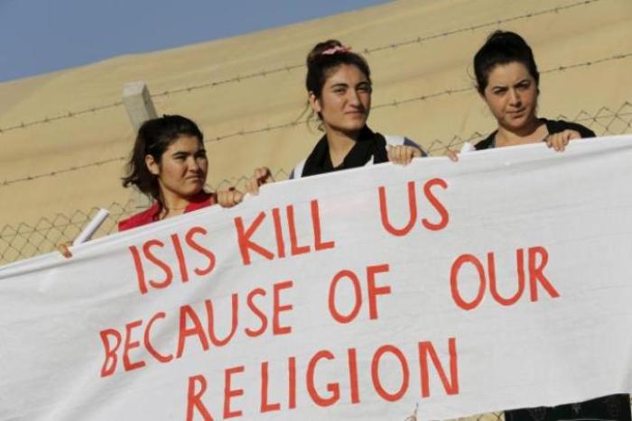 Yazidi refugee women stand behind a banner as they wait for the arrival of United Nations High Commissioner for Refugees Special Envoy Angelina Jolie at a Syrian and Iraqi refugee camp in the southern Turkish town of Midyat in Mardin province, Turkey, on June 20, 2015.