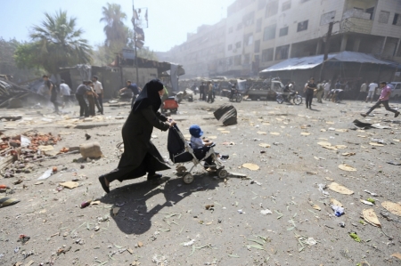 A woman pushes a baby stroller as she rushes away after what activists said were airstrikes by forces loyal to Syria's President Bashar al-Assad on a busy marketplace in Douma, near Damascus, Syria, August 12, 2015.