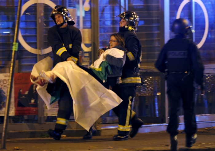 French fire brigade members aid an injured individual near the Bataclan concert hall following fatal shootings in Paris, France, November 13, 2015. At least 30 people were killed in attacks in Paris and a hostage situation was under way at the concert hall in the French capital, French media reported on Friday.