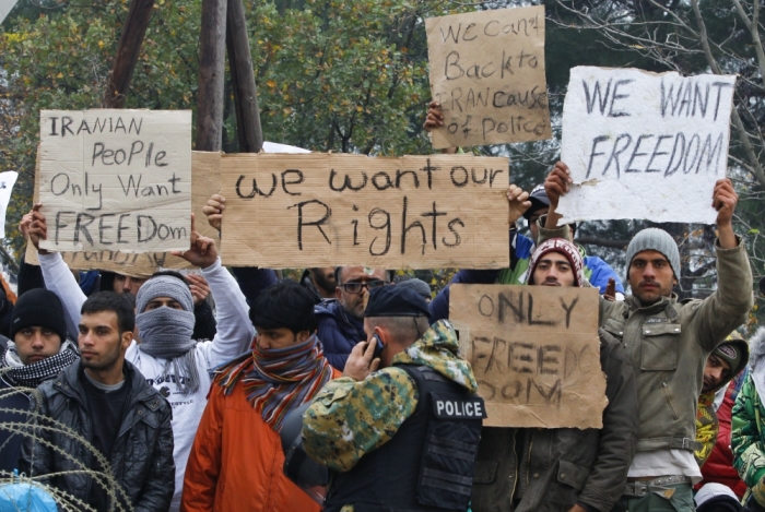 Migrants hold banners as Macedonian policeman stands guard at the border with Greece near Gevgelija, Macedonia, November 20, 2015.