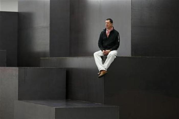 British artist Antony Gormley poses for a photograph on his sculpture 'Model' at a White Cube gallery in London