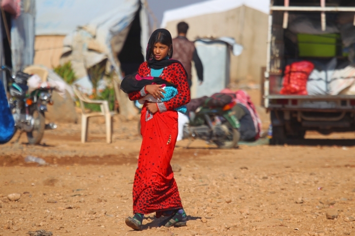 An internally displaced girl holds a child as she walks at a makeshift refugee camp in Sinjar town, in Idlib province, Syria November 20, 2015.