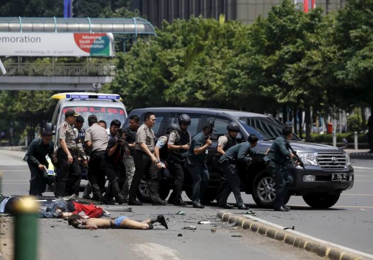 Dead bodies are seen as Indonesian police hold rifles while walking behind a car for protection in Jakarta, January 14, 2016. Several explosions went off and gunfire broke out in the center of the Indonesian capital on Thursday and police said they suspected a suicide bomber was responsible for at least one the blasts.