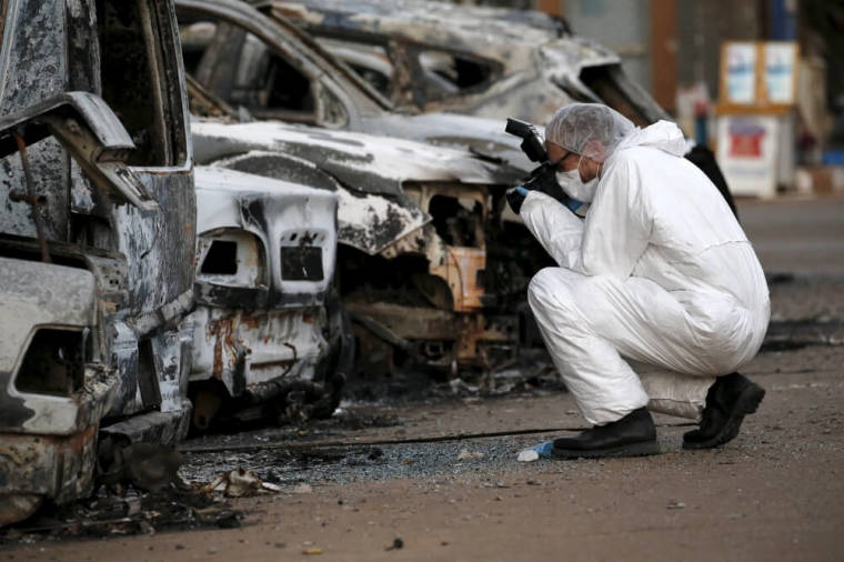 A French police officer photographs burned vehicles outside the Splendid Hotel in Ouagadougou, Burkina Faso, January 17, 2016.