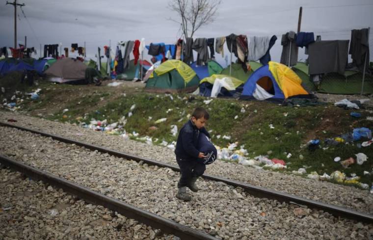 A migrant boy walks along railway tracks at a makeshift camp on the Greek-Macedonian border near the village of Idomeni, Greece March 10, 2016.