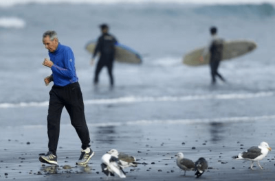 An elderly man exercises with a jog along the beach as surfers head into the ocean in La Jolla, California January 20, 2016