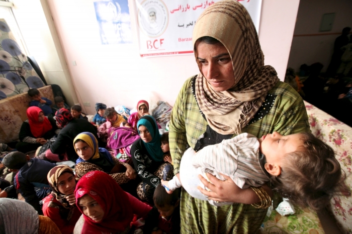 A displaced woman carries her child in a building that is used as a temporary shelter in Makhmour area, southeast of Mosul, Iraq, March 28, 2016.