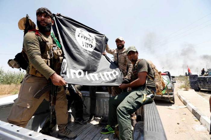 Shi'ite fighters hold an Islamic State flag which they pulled down as they celebrate victory in the town of Garma, Iraq, May 26, 2016.