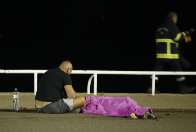 A man sits next to a body seen on the ground July 15, 2016, after at least 30 people were killed in Nice, France, when a truck ran into a crowd celebrating the Bastille Day national holiday July 14.