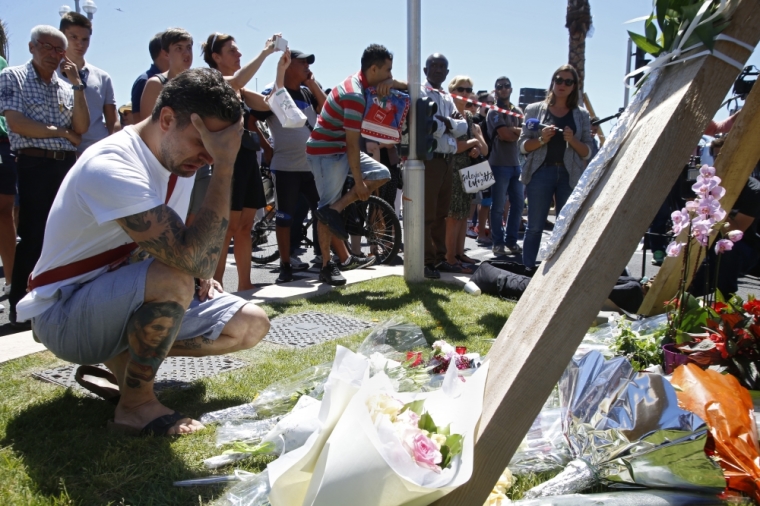 A man reacts near bouquets of flowers near the scene where a truck ran into a crowd at high speed killing scores and injuring more who were celebrating the Bastille Day national holiday, in Nice, France, July 15, 2016.